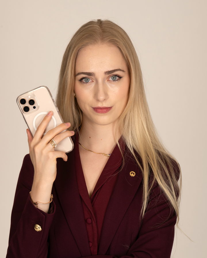 Maureen Evelyn in a burgundy blazer, holding up her phone and looking straight at the camera