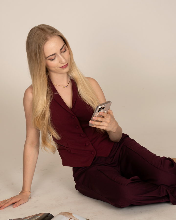 Maureen Evelyn sitting on the floor in a burgundy vest, reading a text thread on her phone